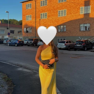 Gul långklänning med oneshoulder - Säljer en elegant gul långklänning med oneshoulder-design. Klänningen har draperad överdel och markerad midja, vilket ger en snygg siluett. 