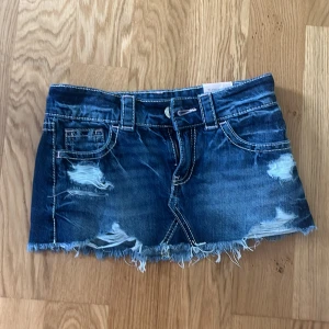 Blå jeanskjol med slitningar Gina Tricot - Supersnygg blå jeanskjol från Gina Tricot i modell x-low. Kjolen är kort med rå, fransig kant och coola slitningar framtill. Klassiska fickor både fram och bak samt bälteshällor. Perfekt för dig som gillar en edgy och trendig stil.