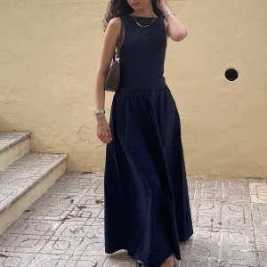 Marinblå ärmlös långklänning - Stilren marinblå långklänning med ärmlös design och rund halsringning. Klänningen har en mjuk, lätt utställd kjol och markerad midja. Perfekt för dig som gillar enkel och elegant stil.