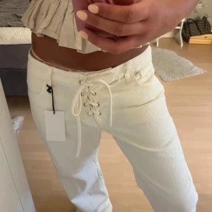 Vita jeans med snörning från Zara - Säljer ett par vita jeans från Zara med snygg snörning framtill istället för vanlig gylf. Byxorna har raka ben, hög midja och klassiska fickor både fram och bak. Materialet är kraftig bomull som ger en clean och fräsch look. De är i storlek 42 men är ganska små i storleken, säljer då de tyvärr var för stora🥲helt nya