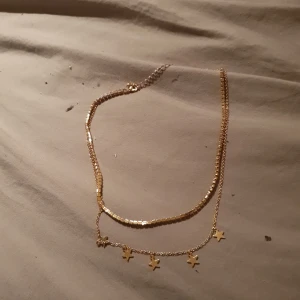 Guldigt halsband med stjärnhängen - Snyggt guldigt halsband med två kedjor, varav den ena har små stjärnhängen som ger en trendig och lekfull look. Perfekt accessoar för att lyfta din outfit med lite extra bling.