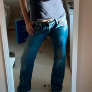 Blå Diesel jeans med röd detalj - Säljer ett par blå jeans från Diesel med snygga röda detaljer vid fickorna och klassisk logga på myntfickan. Jeansen har låg midja och raka ben, tillverkade i slitstarkt denim. Perfekta för dig som gillar en avslappnad men cool stil.