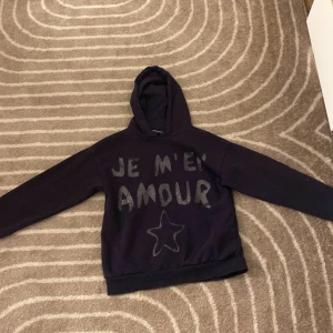 Svart hoodie med text från Gina Tricot -  hoodie från Gina Tricot med glittrig text 'JE M'EN AMOUR' och en stjärna framtill. Tröjan har huva och långa ärmar, super mysig!! ❣️