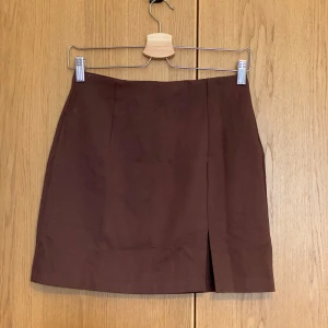 Brun kortkjol från Stradivarius - Kort brun kjol från Stradivarius i stilren design. Skintight passform och en liten slit detalj framtill. Perfekt att matcha med en stickad tröja eller crop top. 