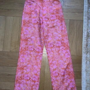Blommiga linnebyxor från Zara - Säljer ett par färgstarka linnebyxor från Zara i storlek S. Byxorna har ett blommigt mönster i rosa och orange, raka ben och normal passform. Materialet är en skön mix av 50% bomull och 50% linne – perfekt för dig som gillar statement-plagg.