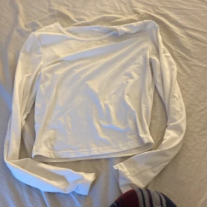 Vit långärmad croppad tröja - En basic vit långärmad tröja med croppad passform. Perfekt att styla med jeans eller kjol för en clean look. Tillverkad i mjuk bomull som känns skön mot huden. Enkel och stilren design utan tryck eller detaljer.