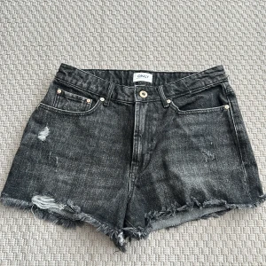 Svarta jeansshorts från ONLY M - Snygga svarta jeansshorts från ONLY med råa, fransiga kanter och slitna detaljer. Klassisk femficksmodell med knapp och dragkedja. Storlek M 