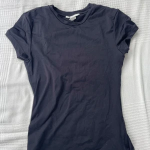 Svart t-shirt från H&M - En basic mörkblå t-shirt från H&M. Modellen är klassisk med rund halsringning och korta ärmar som är slim fit. Perfekt att matcha med jeans eller shorts för en clean look. 
