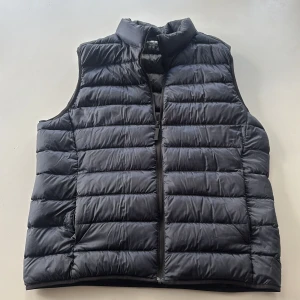Svart dunväst från Uniqlo, M - Säljer en svart, quiltad dunväst från Uniqlo Ultra Light Down. Västen är lätt, har hög krage och dragkedja framtill. Perfekt för lager-på-lager och enkel att bära med sig. Klassisk och stilren design som funkar till det mesta.