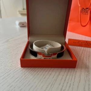  svart och silver armband - Snyggt  armband i silverfärgad metall med svarta detaljer och den ikoniska loggan där fram. Kommer i original orange ask och påse. Perfekt accessoar för att lyfta din outfit med en lyxig touch.funkar till både tjejer o killar.