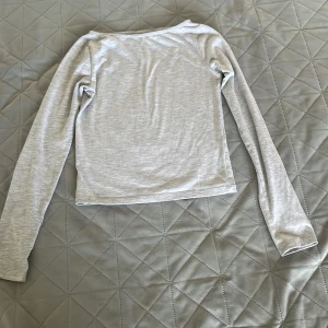 Ljusgrå långärmad tröja från H&M - En basic ljusgrå långärmad tröja från H&M i mjukt bomullsmaterial. Tröjan har en enkel och clean design med rund halsringning och normal passform. Perfekt att matcha med jeans eller kjol för en chill look.