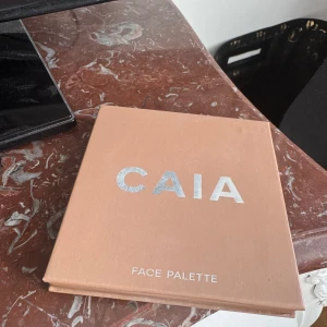CAIA Face Palette med spegel - Säljer en CAIA Face Palette med fyra olika puder: en matt brun contour, en varm bronzer, en intensivt rosa blush och en skimrande persikofärgad highlighter. Paletten har inbyggd spegel och stilren beige förpackning. Perfekt för att skapa en fräsch bas och glow.