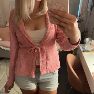 Rosa stickad kofta med knyt från Sincerely Loved - Supersöt rosa stickad kofta från Sincerely Loved i storlek M. Koftan har lång ärm, öppen front och knytband framtill. Den är i ett mjukt, strukturerat material och har en feminin, avslappnad passform. Perfekt att slänga över ett linne eller t-shirt. Denna koftan är i storlek 40/42 men sitter bra på mej som oftast har kläder i 38