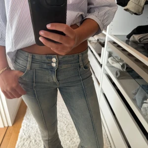 Ljusblå bootcut jeans - Säljer ett par ljusblå jeans med bootcut-modell och snygga pressveck längs benen. Jeansen har dubbla silverfärgade knappar i midjan och klassiska bakfickor. 