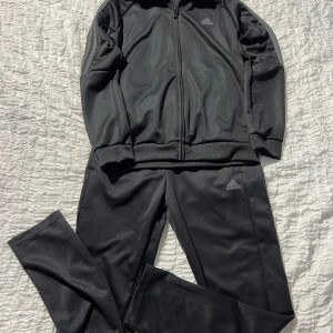 Svarta Adidas mjukisbyxor, stl 152 - Svarta mjukisbyxor från Adidas med klassisk logga på benet. Byxorna har elastisk midja och är gjorda i ett mjukt, syntetiskt material som är perfekt för chill eller träning. Snygg och enkel design som funkar till allt.