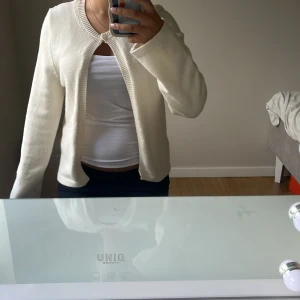 Vit kofta från Gina Tricot - Säljer en stilren vit kofta från Gina Tricot. Den har rund halsringning, lång ärm och stängs med en knapp upptill. Koftan är ribbstickad vid kanterna och är gjord i mjukt material som passar perfekt till lager-på-lager.