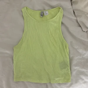 Ljusgul ribbad linnetopp från Hm  - Säljer en ljusgul croppad linnetopp från H&M. Toppen är ribbad och ärmlös med rund halsringning och tight passform. Perfekt för varma dagar eller att styla lager på lager. Superfräsch färg som poppar till outfiten!