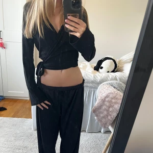 Svart omlottopp från NA-KD - Säljer en svart omlottopp från NA-KD i ribbad bomull. Toppen har långa ärmar, croppad passform och knyts i sidan. 