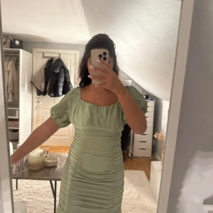 Ljusgrön kort klänning med puffärm - Supersöt ljusgrön kort klänning med puffärmar och rynkade detaljer längs hela klänningen. Den har en fyrkantig ringning och är figurnära med en trendig, romantisk vibe. Perfekt för dig som vill sticka ut med en fräsch färg och snygg passform. Är i storlek L men skulle säga att en M skulle kunna ha den också. Den är använd 1-2 gånger.