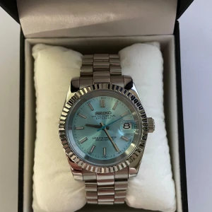 Ljus blå seiko mod date-just - Snygg silverfärgad klocka från Seiko med en stilren design. Urtavlan är ljusblå med datumvisning och klockan har en robust länkarmband i metall. Perfekt för den som gillar en klassisk och tidlös stil. BOXEN INGÅR EJ!!