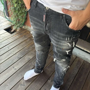 Svarta Dsquared2 jeans med färgstänk - Snygga svarta jeans från Dsquared2 med slitna detaljer och coola färgstänk i vitt, blått och orange. Jeansen har en smal passform och klassisk femficksdesign. Perfekta för dig som vill sticka ut med en edgy streetstyle.