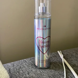 Unicorn Sparkle Body Mist Revolution - Unicorn Sparkle Body Mist från I Heart Revolution med doften Sweet Rainbow. Flaskan är cylinderformad och har en skimrande, holografisk yta med rosa text och hjärtdetalj. Innehåller 236 ml och har en praktisk sprayfunktion. Perfekt för dig som älskar glittriga och söta dofter./ANVÄND NÅGRA GÅNGER⚠️
