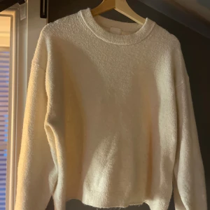 Vit stickad tröja med rund hals - Mysig vit stickad tröja med rund halsringning och ribbade muddar. Tröjan har en enkel och clean look, perfekt att styla med jeans eller kjol. Långärmad modell med lite loose fit för en avslappnad vibe.