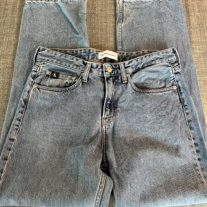Ljusblå jeans från Calvin Klein 90s straight - Säljer ett par klassiska ljusblå jeans från Calvin Klein Jeans med raka ben och normal passform. Jeansen har fem fickor, tydlig CK-logga på bakfickan och är tillverkade i slitstarkt bomullsjeans. Dragkedja i gylfen. Perfekta för en clean och tidlös look. Färgen ser gråare ut på foto, sista bilden är mest rättvis.