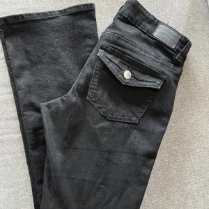 Svarta skinny jeans från Gina Tricot - Svarta skinny jeans från Gina Tricot med klassisk femficksdesign och snygg fickdetalj med lock och knapp bak. Jeansen har normalhög midja och är tillverkade i stretchig bomullsblandning för en bekväm passform. Helt nya!!!!