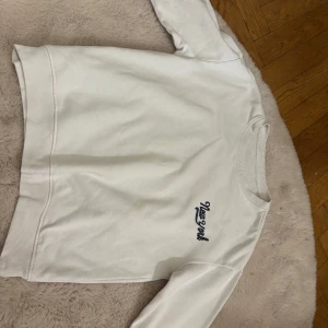 Vit sweatshirt med New York-tryck - Säljer en vit sweatshirt med ett stilrent New York-tryck i mörkblått på bröstet från lager 157 Tröjan har en klassisk rund hals och ribbade muddar vid ärmslut och nederkant. Perfekt för en avslappnad stil. Tror på ett ungefär att den är i storleken 152