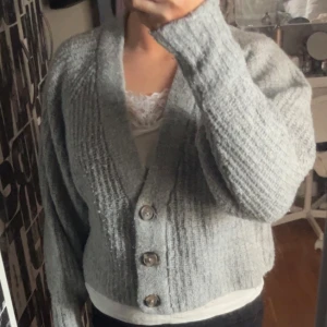 Grå stickad kofta från Gina Tricot storlek S - Mysig grå stickad kofta från Gina Tricot med stora knappar framtill. Den är långärmad. Den är ganska sliten och att den är nopprig. Den är lite kort och är i storlek S