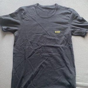 Svart t-shirt från Boss - Snygg svart t-shirt från Boss med liten gul logga på bröstet. Perfekt till sommaren! 
