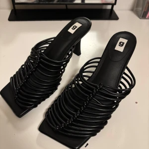 Svarta klackskor med remmar - Snygga svarta klackskor med unika remmar som ger en modern look. Skorna har en fyrkantig tå och en bekväm klackhöjd, perfekt för att lyfta din stil.