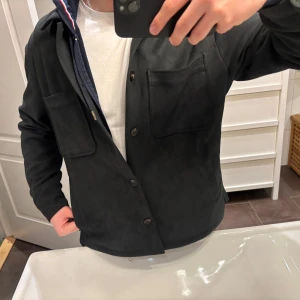 Svart mocka overshirt - Snygg svart mocka overshirt med knappar framtill och två bröstfickor. Perfekt för lager-på-lager-stil och passar till många olika outfits. En stilren och mångsidig jacka för alla tillfällen. Skriv gärna om du har några frågor, priset går att prutas