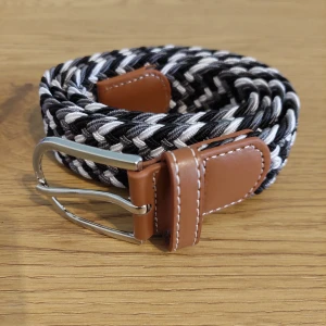 Flätat bälte med läderdetaljer - Snyggt flätat bälte i svart och vitt med bruna läderdetaljer och ett silverfärgat spänne. Perfekt för att ge din outfit en stilren touch.
