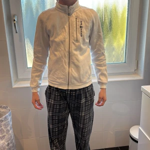 Vit flis från Sail Racing utan huva - Säljer en stilren vit jacka från Sail Racing med dragkedja framtill och broderad logga på bröstet. Jackan har långa ärmar och en hög krage för extra skydd mot vind. Perfekt för vår och höst! Har en liten missfärgning som är nästan osynlig (se bild 3) och en trasig dragkedja i den lilla fickan (bild 4), tröjan är i storlek 150, säljer därför tröjan för det låga priset.