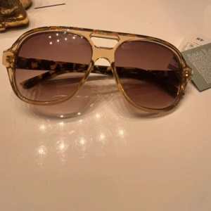 Bruna solglasögon med leopardmönster - Snygga solglasögon med brun tonade glas och en cool leopardmönstrad båge. Perfekta för att ge din stil en extra edge. De har en klassisk aviatorform som aldrig går ur tiden.