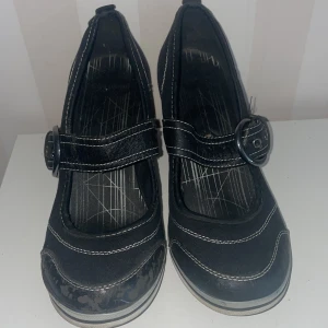 Svarta pumps med spänne - Snygga svarta pumps från Graceland med dekorativt spänne och kontrastsömmar. Klackhöjd 7 cm, slitage se bilder.Skorna har en bekväm klack och rundad tå, vilket ger en stilren look. Perfekta för att ge en elegant touch till din outfit.