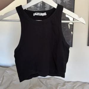 Svart ribbad linnetopp från NA-KD - Snygg svart ribbad linnetopp från NA-KD. Perfekt för en stilren look med sin ärmlösa design och croppade passform. Enkel att matcha med olika outfits.