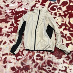 Beige vindjacka från OTP - Säljer en beige vindjacka från OTP med svarta detaljer. Jackan har en dragkedja framtill och långa ärmar. Perfekt för blåsiga dagar och har en sportig look.