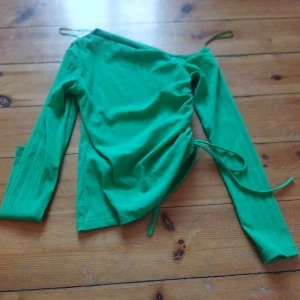 Grön långärmad topp från Gina Tricot - Snygg grön långärmad topp från Gina Tricot med knytning i sidan. Perfekt för att ge en färgklick till din outfit. Toppen har en åtsittande passform och är tillverkad i ett mjukt material. Den är en off shoulder topp