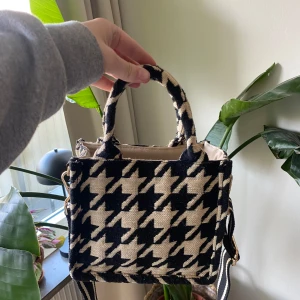Svart och beige rutig handväska från HM - Snygg handväska med ett klassiskt svart och beige rutigt mönster från HM. Väskan har både handtag och en justerbar axelrem för flexibilitet. Väskan är i superfint skick. 