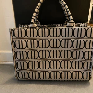 Mönstrad shoppingväska från Don Donna - Snygg shoppingväska från Don Donna med ett unikt mönster i svart och beige. Väskan har två handtag och en praktisk innerficka med dragkedja. Perfekt för att bära med sig allt man behöver under dagen. Säljer väskan och plånboken tillsammans då jag köpte de tills mans man får väskan och plånbok för 250!