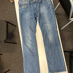 Blå jeans från Diesel - Snygga blå jeans från Diesel med klassisk femficksdesign och knappgylf. Jeansen har en straight passform och är perfekta för en avslappnad stil. Diesel-loggan syns tydligt på bakfickan.