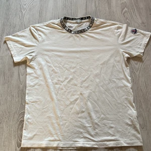Vit t-shirt från Moncler - Säljer en stilren vit t-shirt från Moncler med korta ärmar och en snygg logotypdetalj på kragen. Tillverkad i mjuk bomull för en bekväm passform. Perfekt för en avslappnad look.  Storlek M. Ny pris 2800kr använd 4 gånger.