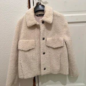 Beige teddyjacka från Zara - Säljer en mysig beige teddyjacka från Zara med knappar framtill. Perfekt för kyliga dagar och ger en trendig look. Jackan har en klassisk krage och är långärmad. Använd 2 gånger, säljer pga för liten🌸🌸