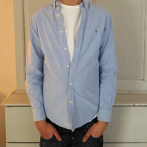 Blå skjorta från Ralph Lauren - Säljer en stilren blå skjorta från Ralph Lauren i slim fit. Skjortan har långa ärmar och knappar framtill. Perfekt för en snygg och avslappnad look. Org pris 1599kr.