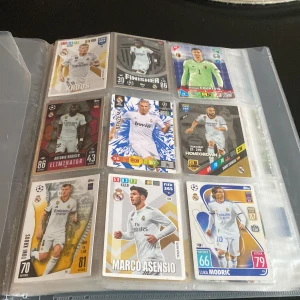 Fotbolls kort - Samling av fotbollskort i ett album med spelare från olika klubbar som Real Madrid, Barcelona, Chelsea, Manchester City, och Liverpool. Inkluderar kort av kända spelare och legender, med olika design och färger. Perfekt för samlare och fotbollsfans.