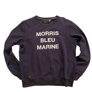 Mörkblå sweatshirt från Morris - Säljer en stilren mörkblå sweatshirt från Morris med texten 'MORRIS BLEU MARINE' på framsidan. Tröjan har långa ärmar och ribbade muddar vid ärmslut och nederkant. Perfekt för en avslappnad stil.