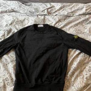 Svart tröja från Stone Island Junior - Säljer en stilren svart tröja från Stone Island Junior. Tröjan har långa ärmar och ett ikoniskt märke på ärmen. Perfekt för en casual look. det  är en junior och storleken är 12yr och 156cm, köpte den för ungefär 1000kr, inte använd mycket, måste ta bord loggan innan man lägger den i tvättmaskin och torktumlare 